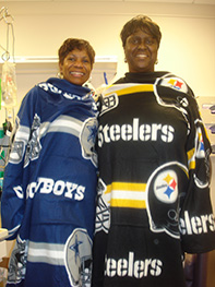 Joyce visits her best friend “Stu” in the hospital dressed in their rival football team outfits